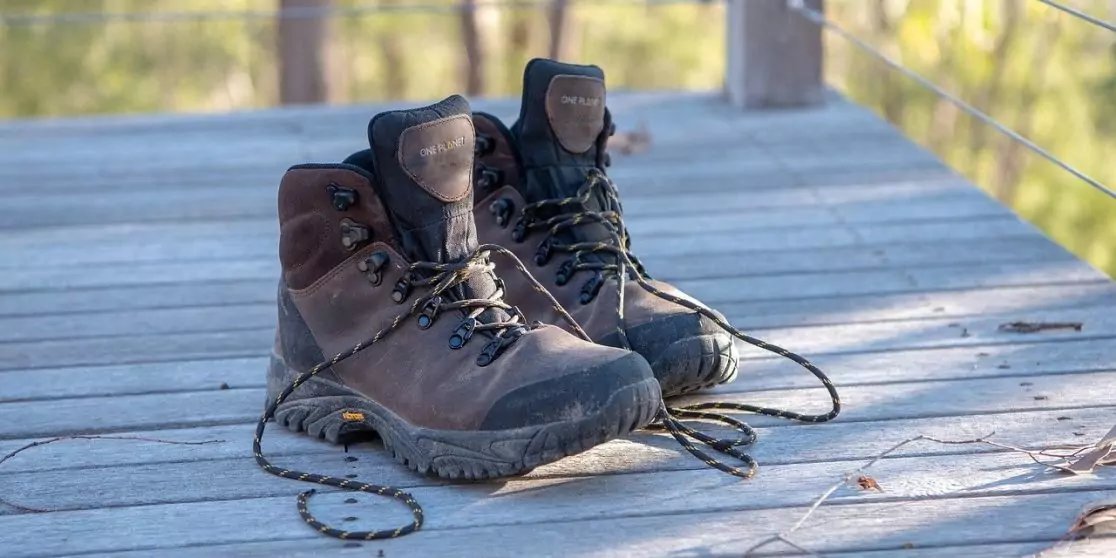 Ein Paar braune Wanderschuhe mit losen Schn&uuml;rsenkeln auf einem Holzsteg; Gel&auml;nder und verschwommene Vegetation im Hintergrund