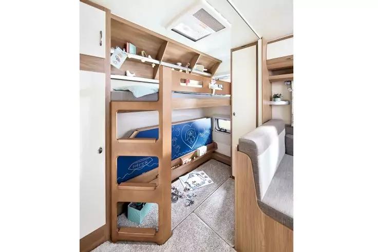 Innenraum eines Wohnmobils mit zwei Etagenbetten, Holzleiter, blauen Matratzen und offenem Stauraum