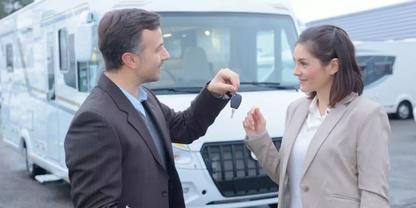 Mann &uuml;bergibt Schl&uuml;ssel an Frau vor einem wei&szlig;en Wohnmobil auf einem Parkplatz