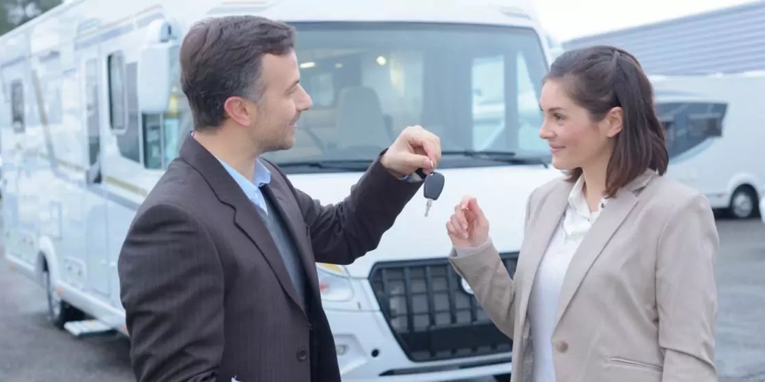 Mann &uuml;bergibt Schl&uuml;ssel an Frau vor einem wei&szlig;en Wohnmobil auf einem Parkplatz