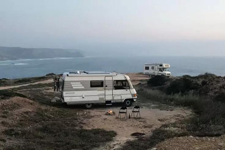 Zwei Wohnmobile auf einer Klippenk&uuml;ste, zwei Personen neben dem vorderen Wohnmobil, zwei Klappst&uuml;hle, Meer im Hintergrund