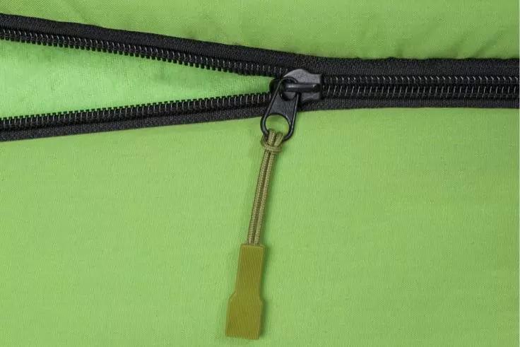 Nahaufnahme eines schwarzen Rei&szlig;verschlusses auf hellgr&uuml;nem Stoff mit gr&uuml;ner Gummilasche und Metallring