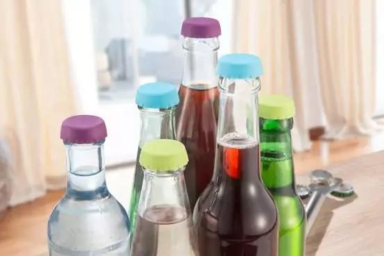 Mehrere Glasflaschen mit bunten Deckeln auf einem Tisch, helle Vorhänge im Hintergrund