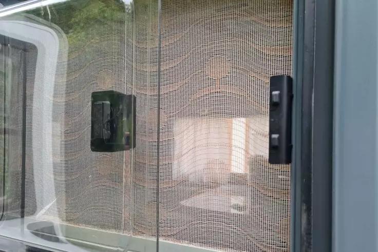 Glasfläche mit feinem Netzgitter, zwei schwarze rechteckige Griffe, unscharfe Innenraumspiegelung