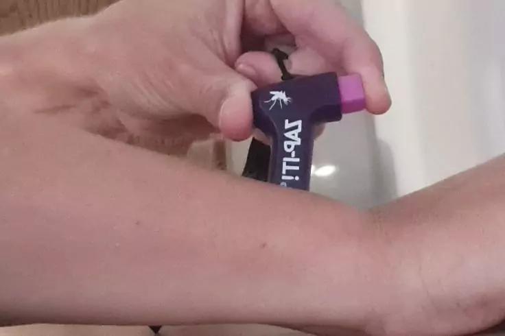 Hand hält kleines lila Gerät mit pinker Kappe an innerem Unterarm