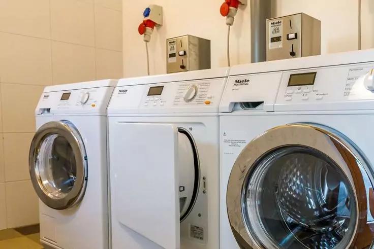 Drei wei&szlig;e Frontlader-Waschmaschinen nebeneinander in einem Waschraum, mit runden Bullaugen und Bedienfeldern oben