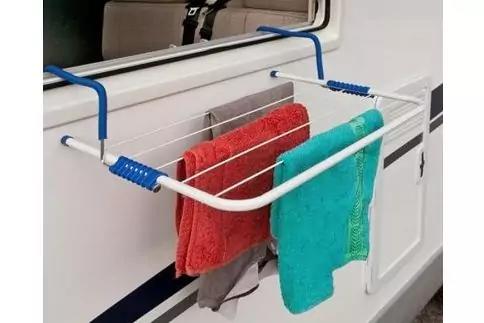 Ausklappbarer wei&szlig;er W&auml;schest&auml;nder an der Au&szlig;enwand eines wei&szlig;en Fahrzeugs mit Fenster, darauf ein rotes Handtuch, ein t&uuml;rkisfarbenes Handtuch und ein graues Kleidungsst&uuml;ck