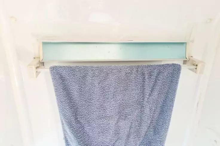 Blaues, gemustertes Handtuch h&auml;ngt &uuml;ber einer wei&szlig;en Stange vor einem kleinen rechteckigen hellblauen Glaseinsatz in einer wei&szlig;en Wand