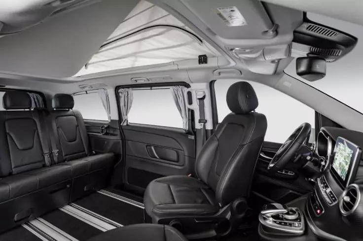 Innenraum eines Fahrzeugs mit schwarzen Ledersitzen, Fahrersitz, gedrehtem Beifahrersitz, Dreisitzer-R&uuml;ckbank, Mittelgang, gro&szlig;er Dachluke, Seitenvorh&auml;ngen und Armaturenbrett mit Touchscreen