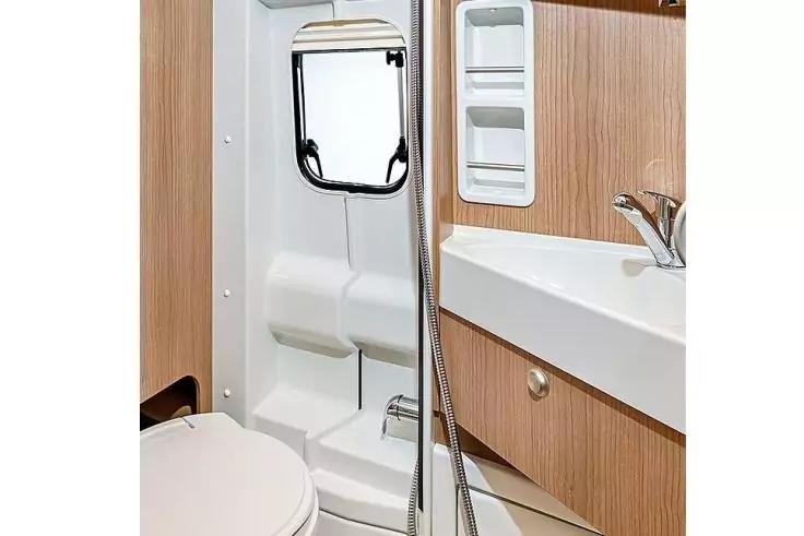 Toilette, Waschbecken mit Armatur, Duschkopf an Schlauch, Holzschrankfronten, kleines rechteckiges Fenster