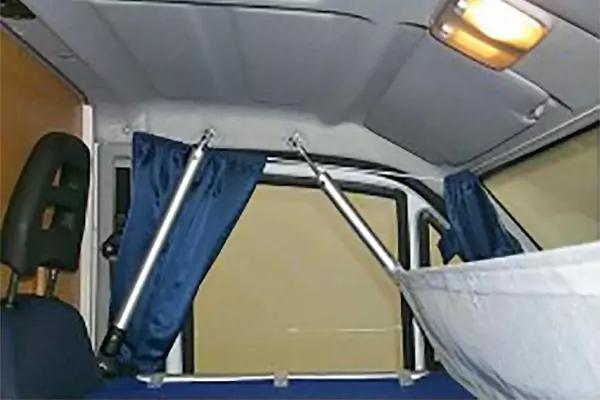 Innenraum mit Sitzkopfst&uuml;tze links, Fenster mit beigem Rollo, zwei blaue Vorh&auml;nge an silbernen Stangen, Deckenleuchte oben rechts, h&auml;ngender wei&szlig;er Stoff rechts