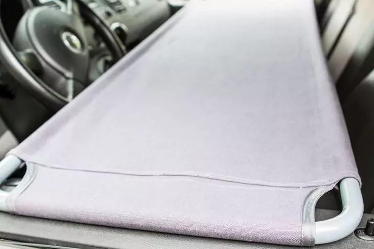 Hellviolettes Stofftuch mit wei&szlig;en Kunststoffgriffen quer im Auto gespannt; Lenkrad und Armaturenbrett im Hintergrund sichtbar