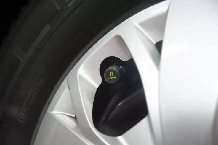 Nahaufnahme eines Autoreifens und einer silbernen Felge mit schwarzer Ventilkappe, auf der ein gelbes "R" steht