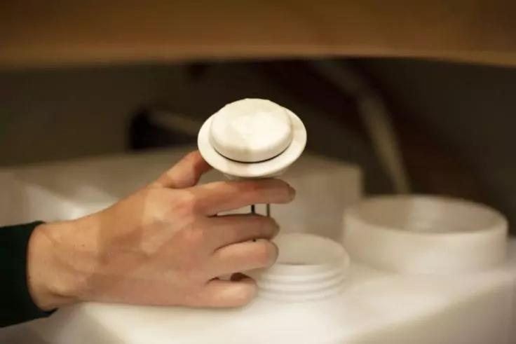 Hand hält rundes weißes Plastikteil über die Öffnung eines weißen Behälters, ein Deckel liegt daneben, Hintergrund unscharf