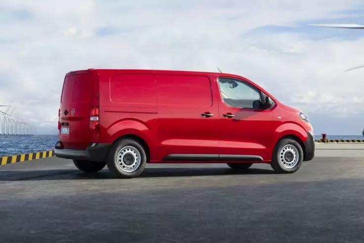 Roter Lieferwagen, Seitenansicht, geparkt auf gepflasterter Fl&auml;che am Wasser; Windr&auml;der im Hintergrund, bew&ouml;lkter Himmel