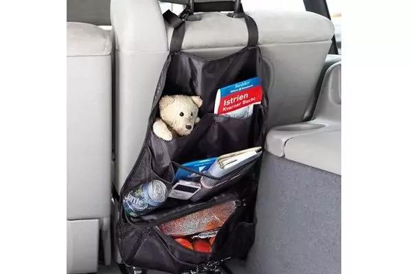 Schwarzer H&auml;ngesack am Vordersitzr&uuml;cken mit Pl&uuml;schteddy, rot-blauer Box, Wasserflasche, Heft/Buch und orangefarbener Kleidung