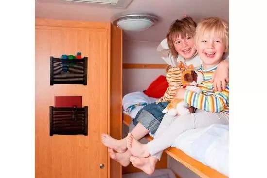 Zwei lachende Kinder auf der oberen Etage eines Etagenbetts in einem holzverkleideten Raum, sie halten ein Stofftier, barfu&szlig;es Herabh&auml;ngen der F&uuml;&szlig;e