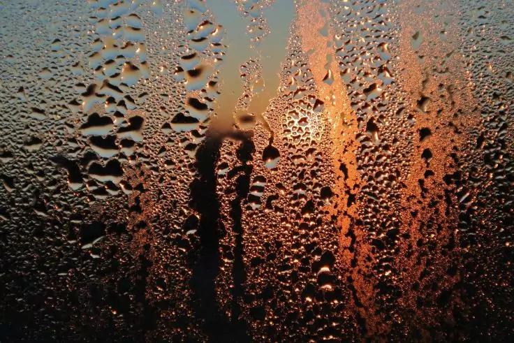 Fensterscheibe mit Wassertr&ouml;pfchen und orangefarbenem Licht im Hintergrund