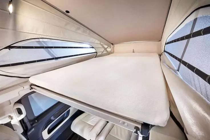 Innenraum mit Matratze auf Plattform, seitliche Fenster mit Verdunkelblenden, Polstersitze darunter und Deckenleuchte