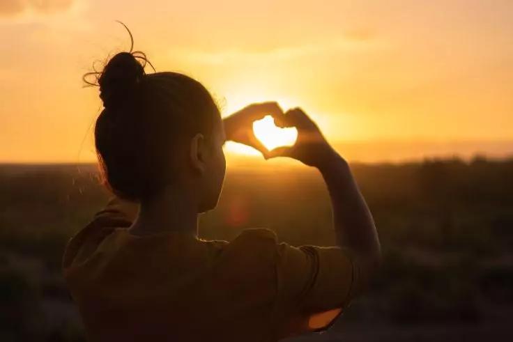 Silhouette einer Person, die bei Sonnenuntergang mit den Händen ein Herz formt
