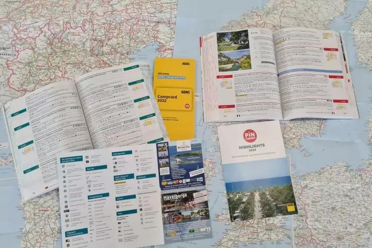 Auf einer Landkarte liegen mehrere ge&ouml;ffnete Brosch&uuml;ren, Hefte und Faltbl&auml;tter, ein kleines gelbes Heft und Brosch&uuml;ren mit Fotos und Text sind sichtbar