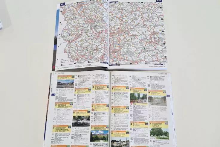 Aufgeschlagenes Heft auf wei&szlig;er Fl&auml;che; obere Doppelseite zeigt eine Stra&szlig;enkarte, untere Seite zeigt Spalten mit Textfeldern und kleinen Fotos