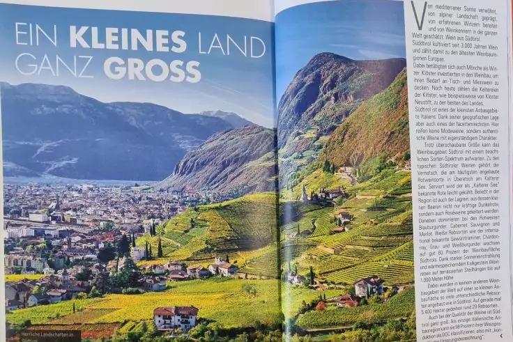 Magazin-Doppelseite mit Panoramafoto: links eine Stadt im Tal, mittig gestufte gr&uuml;ne H&uuml;gel mit verstreuten H&auml;usern, im Hintergrund Berge und blauer Himmel; rechts eine Textspalte; Falz in der Bildmitte sichtbar