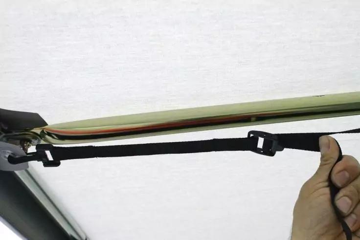 Hand h&auml;lt schwarzen Gurt mit Kunststoffverschluss, befestigt an einem Metallrahmen unter einem gr&uuml;nen Stoff