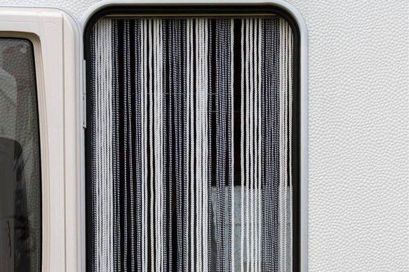 Fenster mit vertikalen schwarz-wei&szlig;en F&auml;den hinter Glas; kleines rechteckiges Papier innen sichtbar; rechts strukturierte wei&szlig;e Fl&auml;che