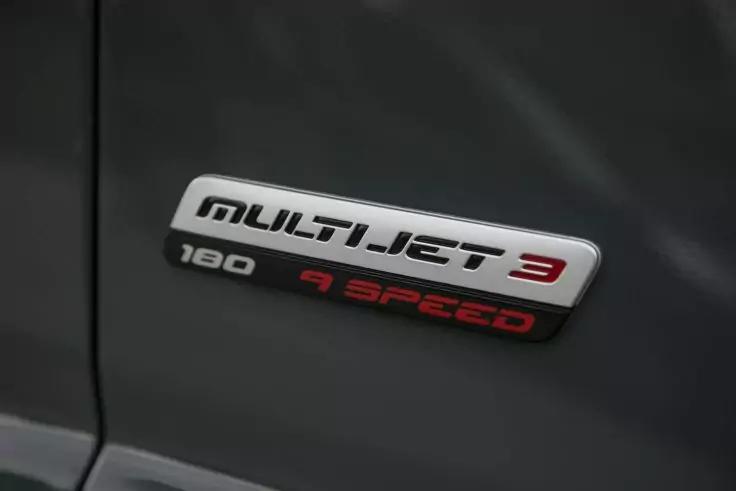 Chromfarbener Fahrzeugschriftzug auf dunkelgrauem Blech: "MULTIJET 3" mit roter "3", darunter links "180" und rechts "7 SPEED"