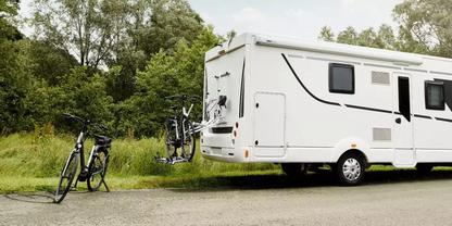 Wei&szlig;es Wohnmobil am Stra&szlig;enrand; zwei Fahrr&auml;der auf einem Heck-Fahrradtr&auml;ger und ein Fahrrad steht neben dem Fahrzeug; Gras und B&auml;ume im Hintergrund