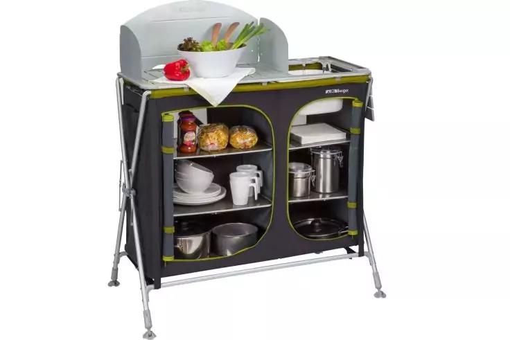 Freistehendes, tragbares K&uuml;chenm&ouml;bel auf Metallbeinen mit zwei runden offenen F&auml;chern; darin Teller, Tassen, T&ouml;pfe, Pfannen und Gew&uuml;rzgl&auml;ser; oben Arbeitsfl&auml;che mit Sp&uuml;le, Wasserhahn, Schneidebrett und Gem&uuml;se