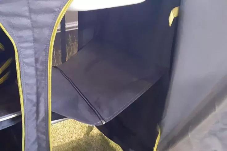 Dunkler Stoff mit gelber Einfassung, ge&ouml;ffnete Seiten&ouml;ffnung und eine Stoffablage, gr&uuml;ner Rasen darunter sichtbar