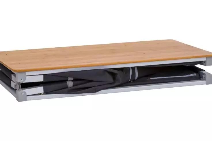 Rechteckige Holzplatte auf silbernem Metallgestell, darunter zusammengefalteter schwarzer Stoff mit Gurten