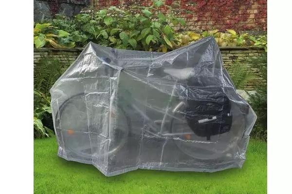 Fahrrad unter transparenter Abdeckung auf Rasen vor einer Backsteinmauer mit Pflanzen