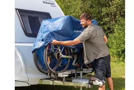 Mann bedeckt zwei Fahrr&auml;der auf dem Hecktr&auml;ger eines Wohnwagens mit einer blauen Plane