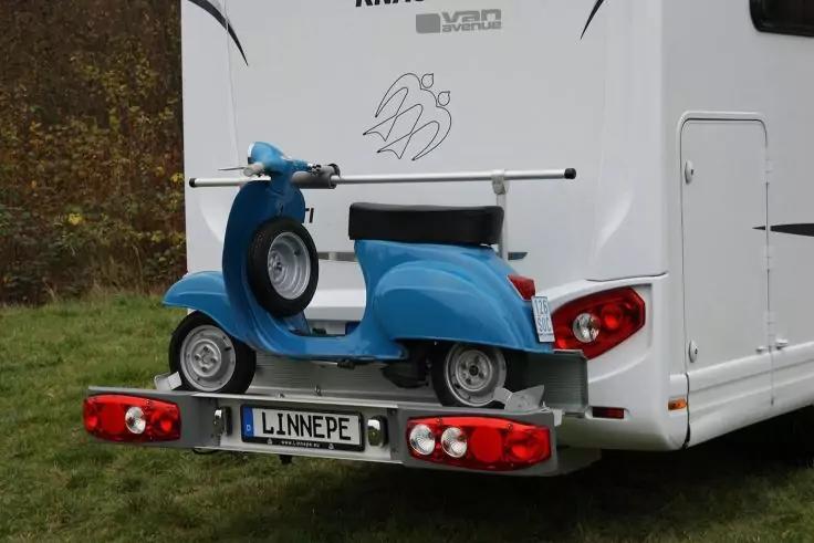 Blauer Motorroller auf Hecktr&auml;ger eines wei&szlig;en Wohnmobils; Kennzeichen 'LINNEPF'; Gras und B&auml;ume im Hintergrund