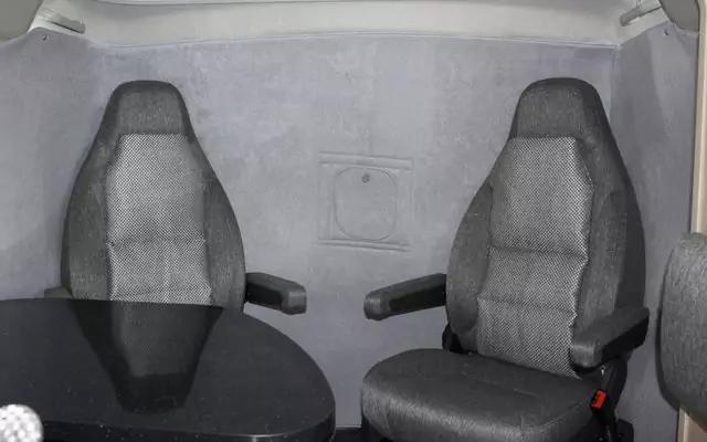 Zwei graue gepolsterte Sitze mit Armlehnen, links ein runder schwarzer Tisch, hellgraue gepolsterte R&uuml;ckwand mit quadratischer Klappe, rote Gurtverschluss am rechten Sitzrand