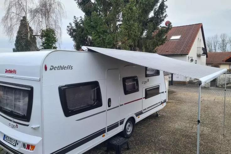 Wei&szlig;er Dethleffs-Caravan mit ausgefahrener Markise auf Kiesplatz, H&auml;user und B&auml;ume im Hintergrund, bew&ouml;lkter Himmel