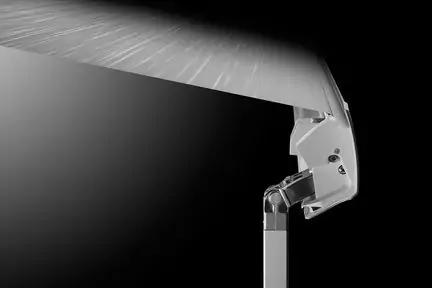 Nahaufnahme eines metallischen Gelenkarms mit Befestigungsplatte, befestigt an einer gerippten, hell beleuchteten flachen Oberfl&auml;che; schwarzer Hintergrund