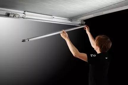 Eine Person steht unter einer ge&ouml;ffneten Garagent&uuml;r und h&auml;lt eine Metallstange an die Innenseite der T&uuml;r