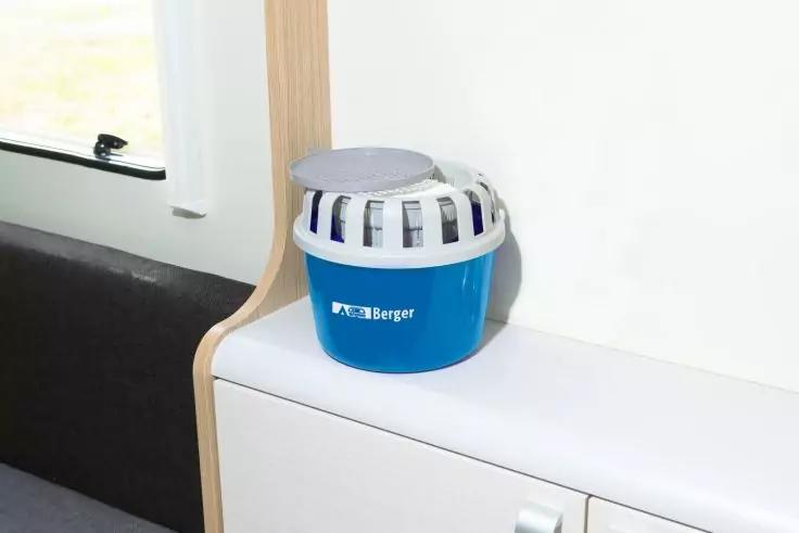 Blaues rundes Kunststoffgefäß mit weißem Gitterdeckel und weißer Aufschrift "Berger", auf einer weißen Ablage neben einem Fenster und einer dunklen Sitzfläche