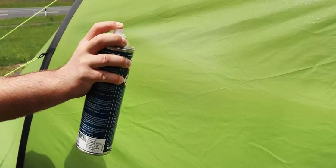 Hand h&auml;lt eine schwarze Spraydose vor gr&uuml;nem Stoff