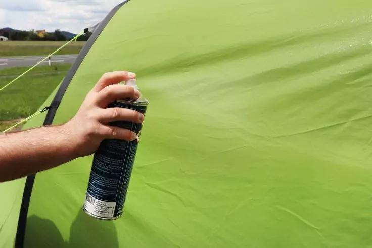 Hand h&auml;lt eine Spr&uuml;hdose neben gr&uuml;nem Zeltstoff auf einer Wiese