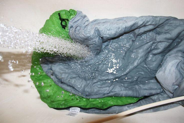 Gefalteter grauer Stoff mit gr&uuml;nem Innenrand in einer Badewanne, ein Wasserstrahl spritzt darauf