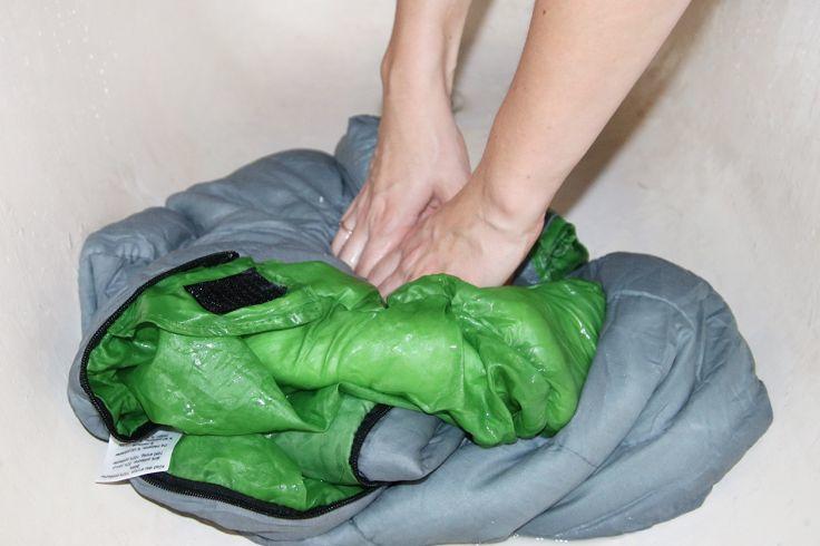 Zwei H&auml;nde wringen eine nasse gr&uuml;ne Steppjacke &uuml;ber einer grauen W&auml;schewanne