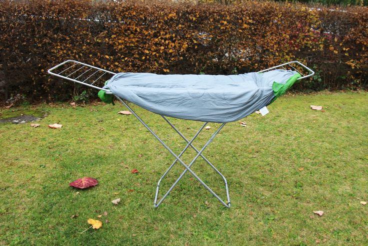 Metall-Klappw&auml;schest&auml;nder auf Rasen mit hellblauem Tuch, an den Enden mit gr&uuml;nen Klammern; Hecke im Hintergrund