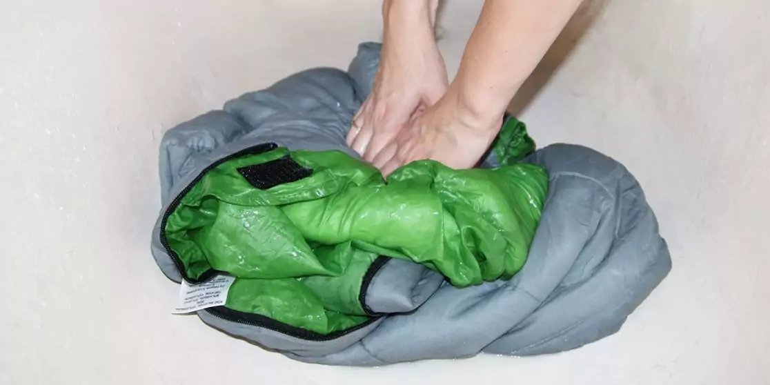 Zwei H&auml;nde dr&uuml;cken eine gr&uuml;ne Steppjacke in eine graue Tasche