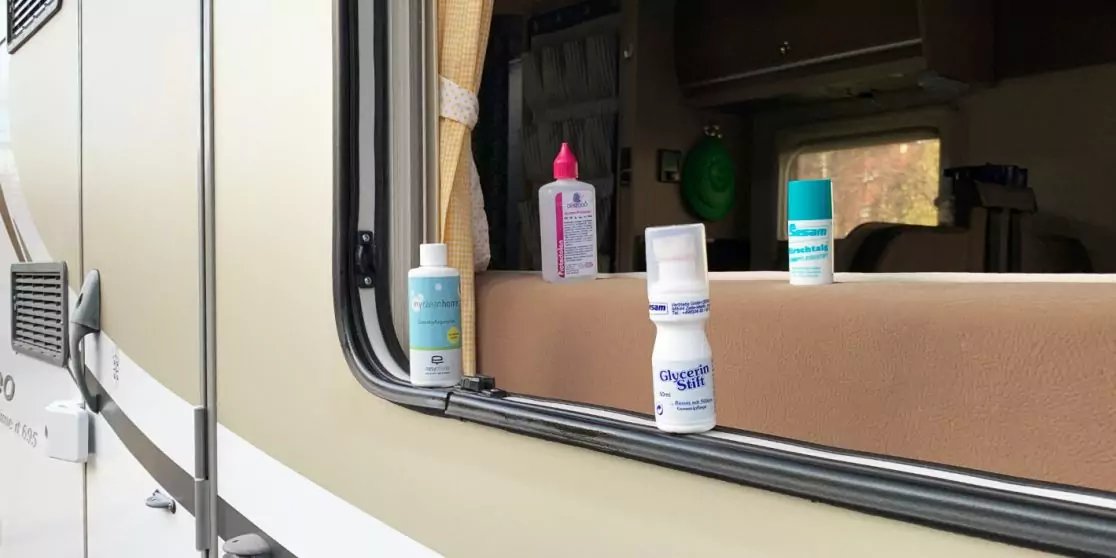 Vier kleine Plastikflaschen auf der Fensterbank eines ge&ouml;ffneten Wohnmobilfensters; Innenraum des Wohnmobils im Hintergrund