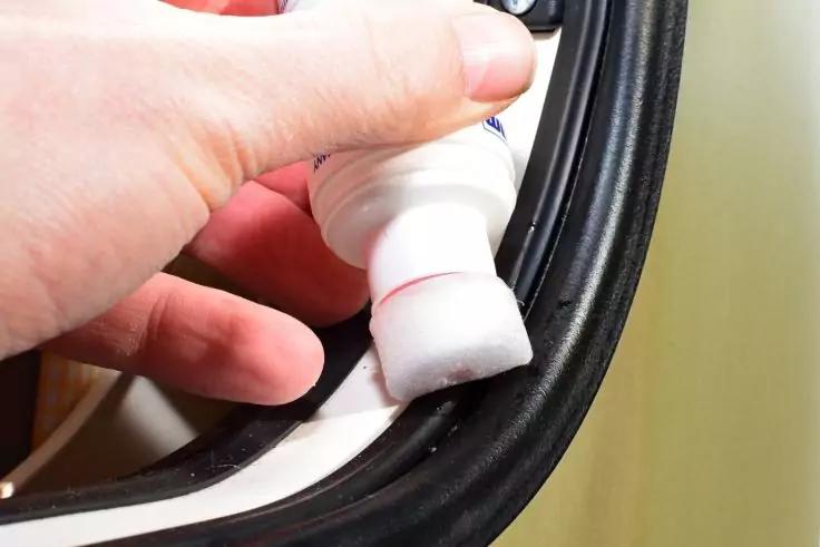 Hand h&auml;lt wei&szlig;e Flasche mit Schaumstoff-Applikator; Schaum auf schwarzem Gummidichtungsrand